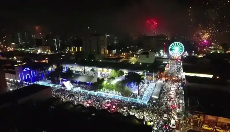 Pessoas nas ruas, roda-gigante iluminada e fogos de artifício. 