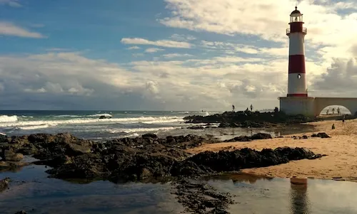 praia de itapuã fotos com Pedras no primeiro plano e farol ao fundo. 