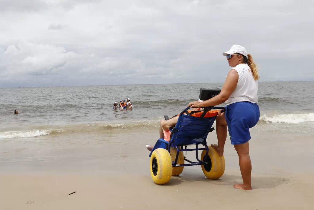 Mulher empurra cadeira de rodas anfíbia para o mar.