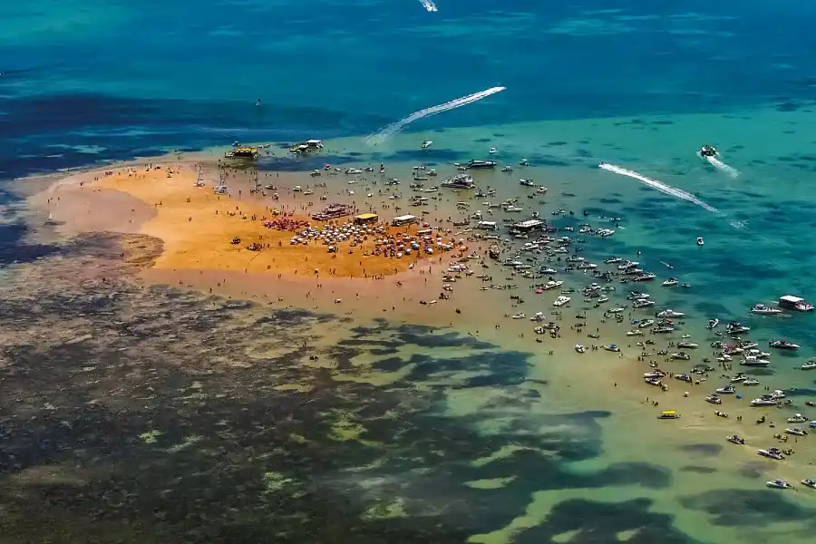 barcos e turistas no meio do mar para observar o banco de areia avermelhada.