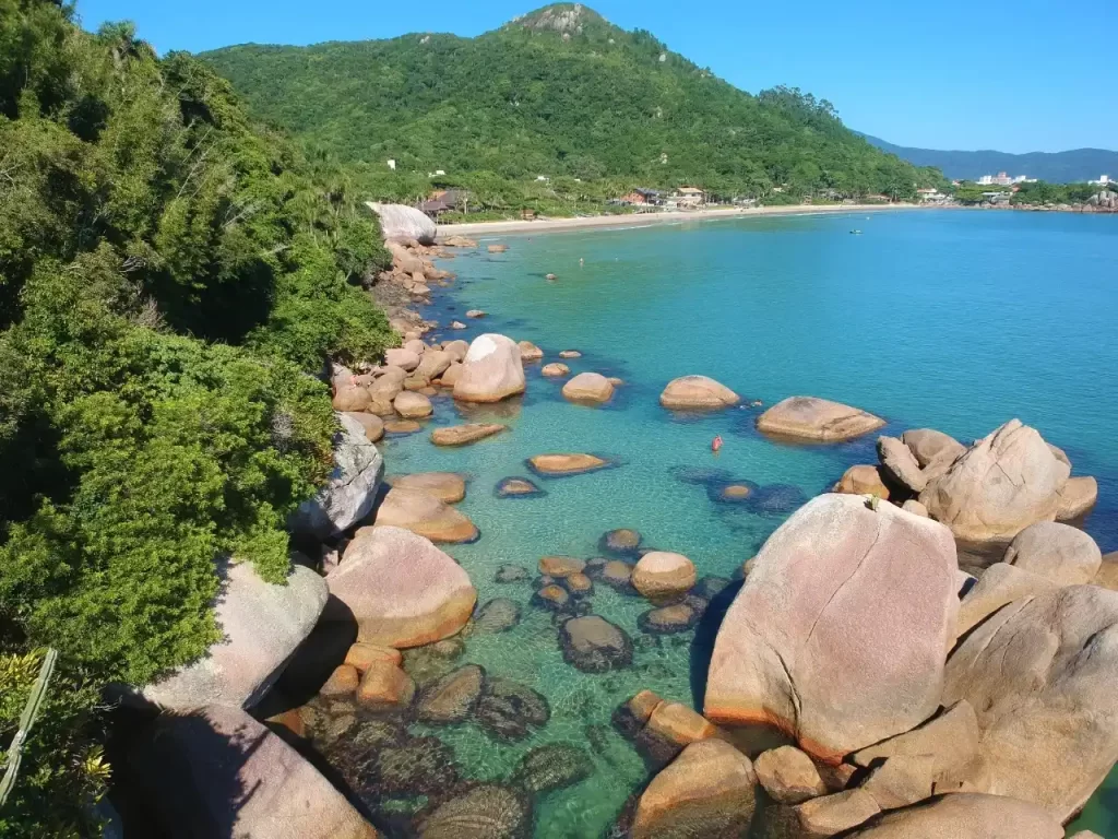 Praia de águas claras, com rochas que formam piscinas naturais.